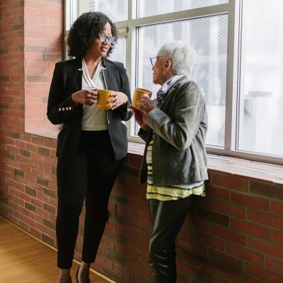 A Woman in Black Blazer Talking to the Woman in Gray Blazer while Standing Near the Window